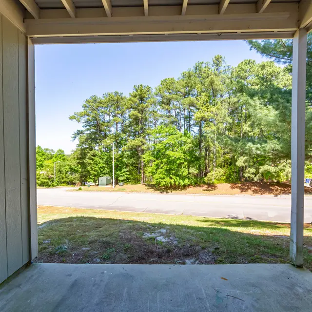 A view from a front porch showing a clear sky, green trees, and a street in the distance.