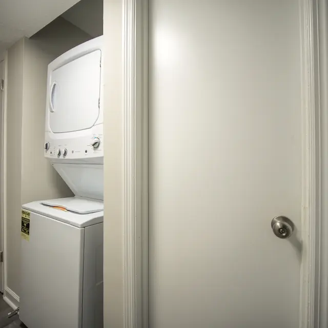 A view of a laundry room featuring a stacked washer and dryer next to a closed white door.