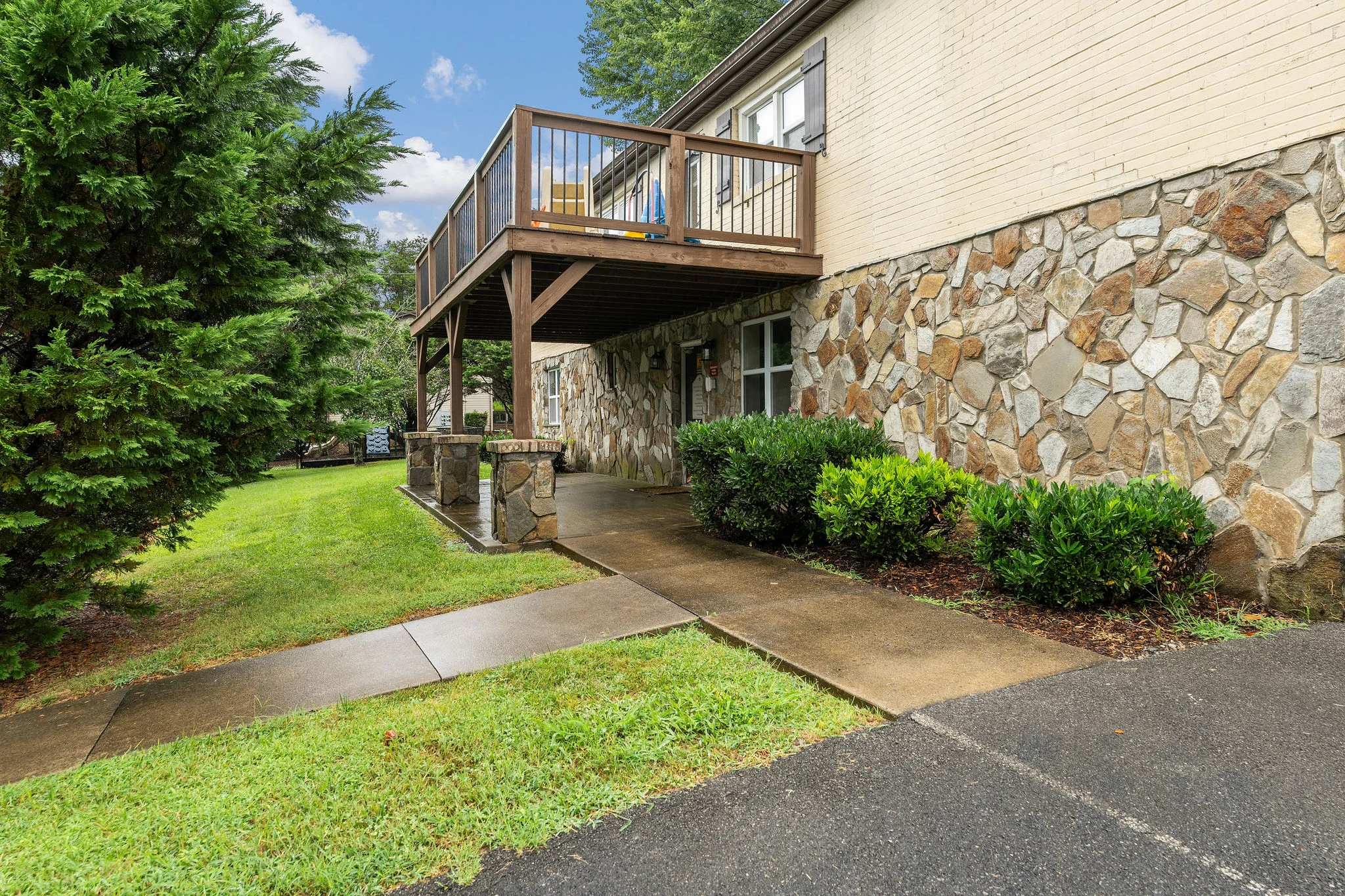 House Exterior with Stone Wall and Balcony Exterior view of a house featuring a stone wall and a wooden balcony overlooking a grassy area.