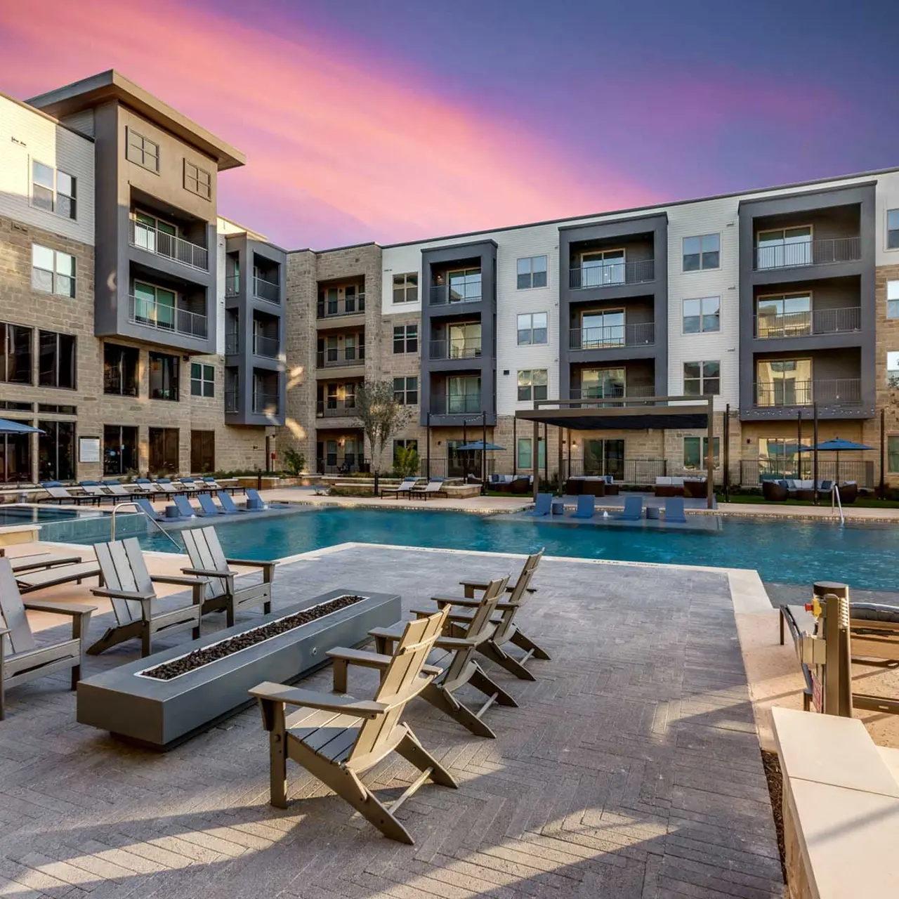 Relaxing Pool Area at Modern Apartments A tranquil pool area surrounded by modern apartment buildings during sunset, featuring lounge chairs and umbrellas.