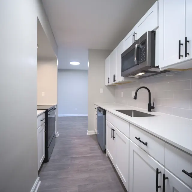 A modern kitchen featuring white cabinets, stainless steel appliances, and a sleek countertop. The kitchen has a gray tile floor and a neutral wall color, creating a bright and airy atmosphere.