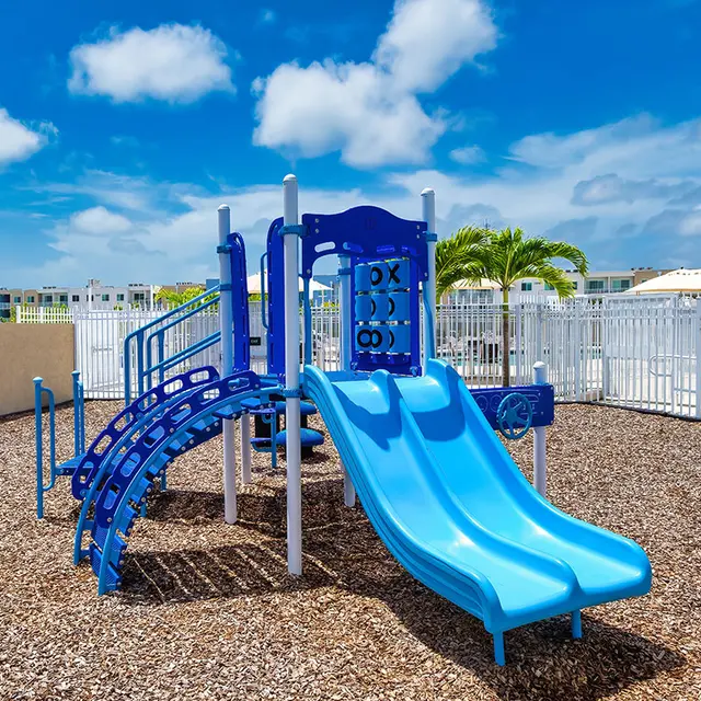 A blue playground with slides and climbers, surrounded by a white fence.