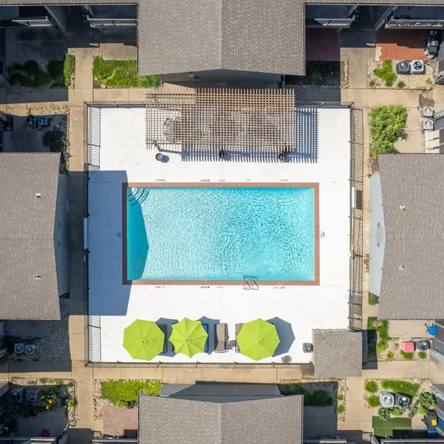 Aerial view of an apartment complex with a swimming pool in the center, surrounded by lounge chairs and green umbrellas.