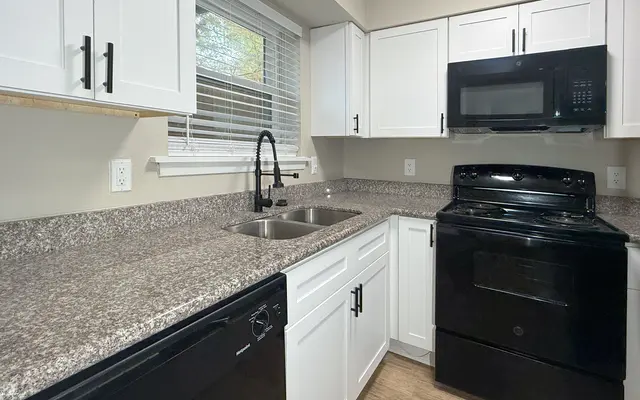 A modern kitchen featuring white cabinets, granite countertops, and black appliances including a microwave and stove.