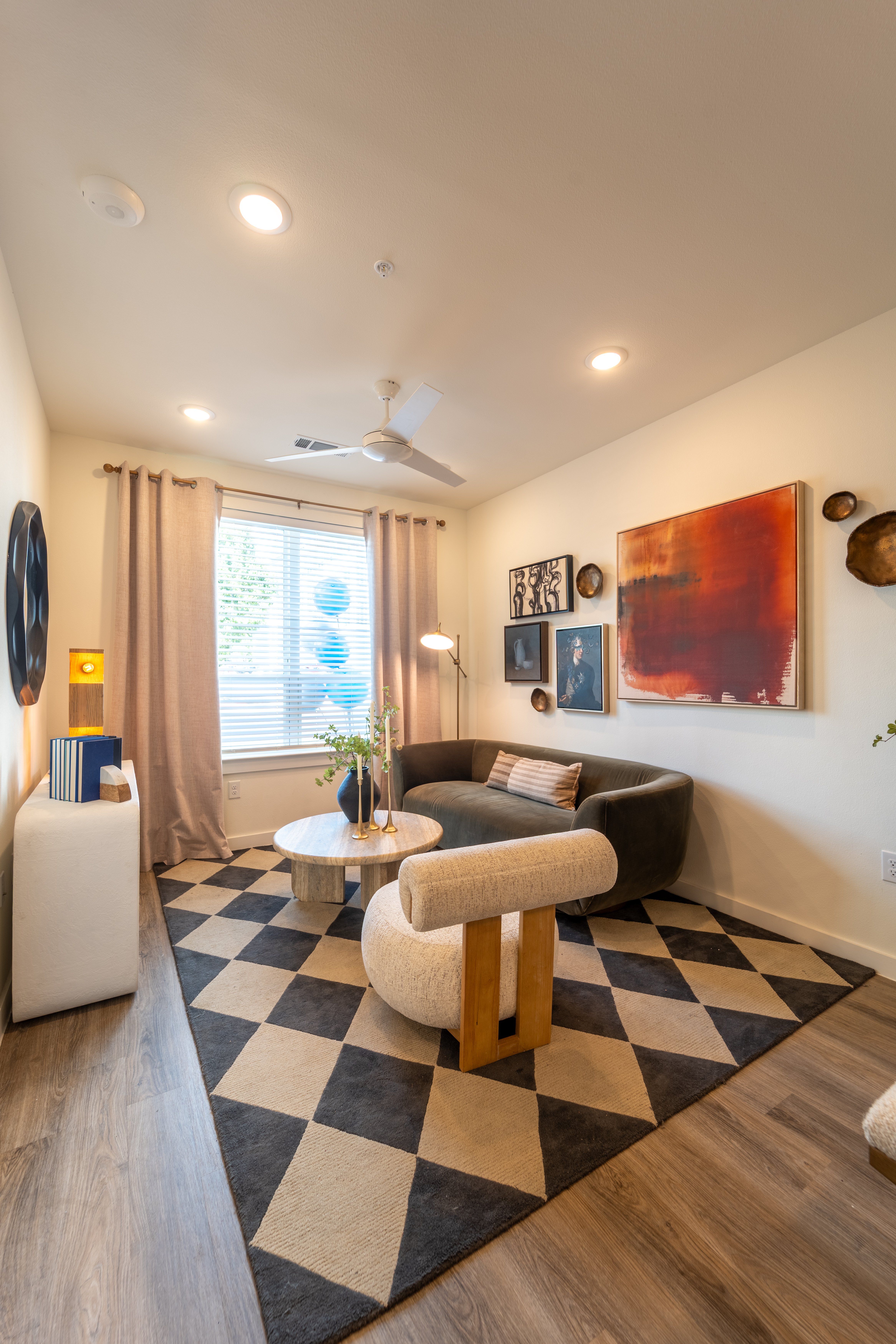 Modern Living Room Design A modern living room featuring a dark circular sofa, round coffee table, and a decorative rug with a geometric pattern. Artwork adorns the walls, and natural light enters through a window with sheer curtains.