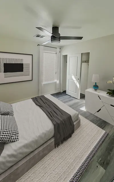 Raymond Place 5 Bedroom Townhouses in South Phoenix AZ - Raymond Place - Furnished Bedroom with Wood Flooring, Bed, White Rug, White Dresser, Lamp, Plants, Ceiling Fan, Mounted Wall Art, Window, and Large Closet with Sliding Doors