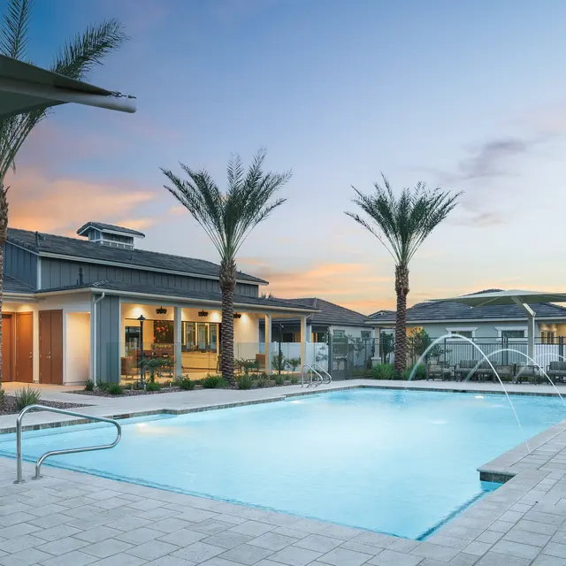 A serene pool area surrounded by palm trees and modern buildings, with a sunset sky and gentle water features.