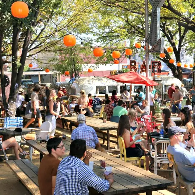 Truck Yard outdoor bar with food trucks and people sitting at picnic tables and talking to friends