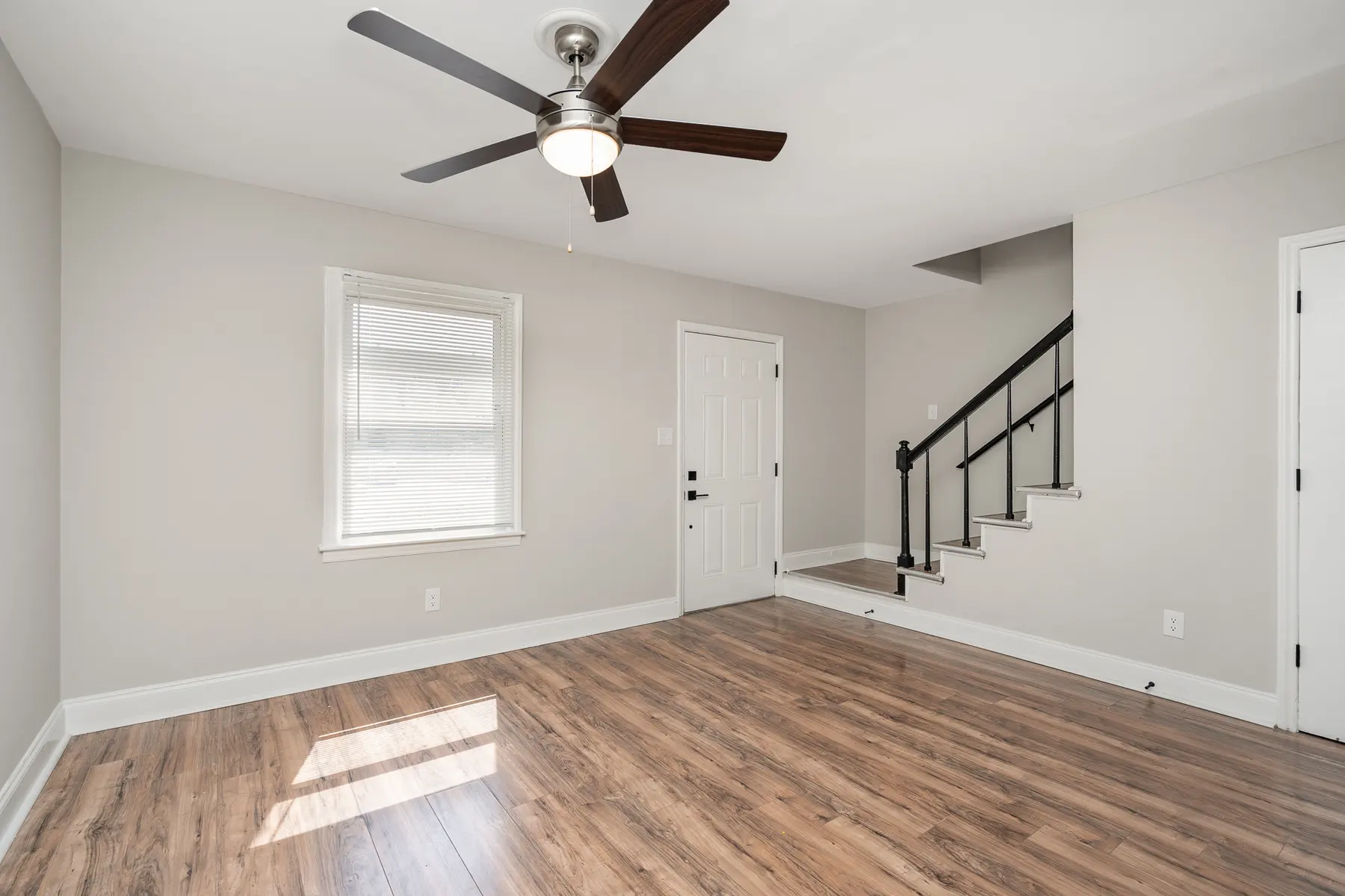 Interior of a living room with a ceiling fan, wooden flooring, and a staircase.