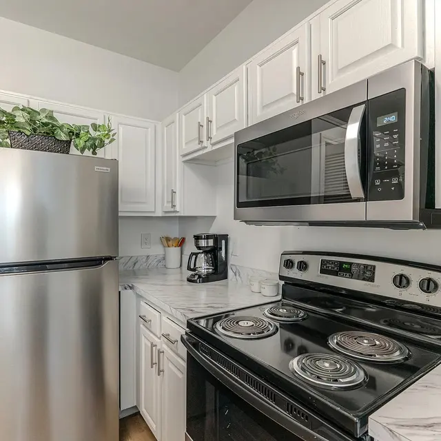 A modern kitchen with stainless steel appliances, including a refrigerator, microwave, and stovetop, paired with white cabinets and marble countertops.