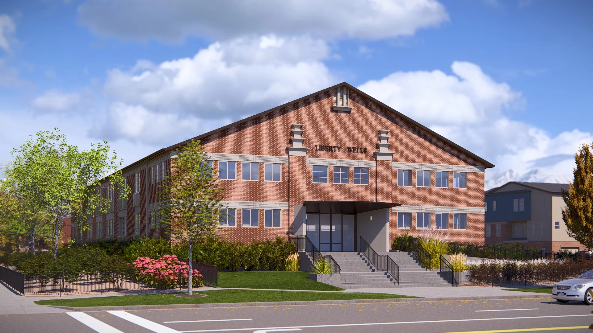 Liberty Well Building A three-story brick building with large windows, named 'Liberty Well', surrounded by trees and shrubs, under a partly cloudy sky.