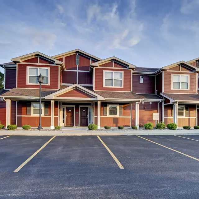 A modern townhouse with red siding and multiple levels, featuring a parking area in front.