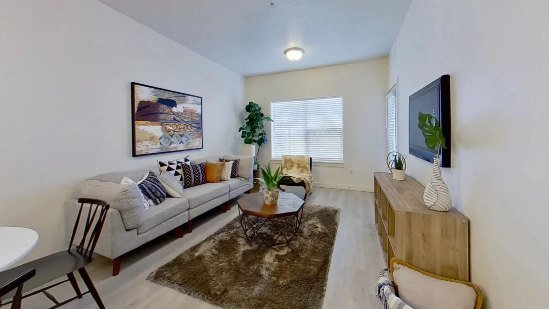 Modern Living Room Interior A cozy living room featuring a light-colored sofa with decorative throw pillows, a coffee table on a plush rug, and a plant in the corner. There is a piece of artwork on the wall and a media console with a small plant decoration.