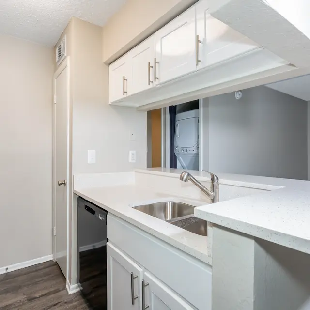 Modern kitchen with white cabinetry, a sink, and a black refrigerator in a light-colored apartment.