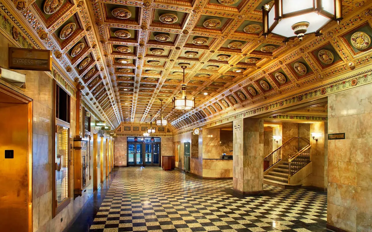An ornate hallway with a beautifully decorated ceiling, featuring intricate patterns and designs, and a checkered floor.
