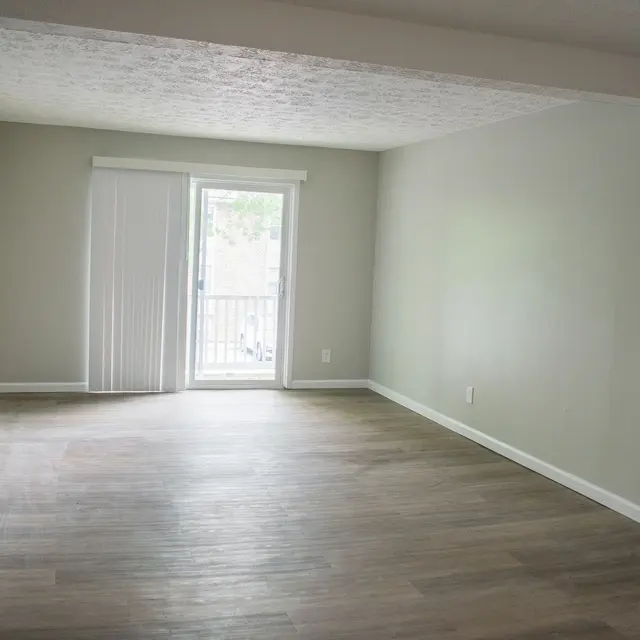 Empty room with light-colored walls and wooden flooring, featuring a sliding glass door leading to an outdoor space.