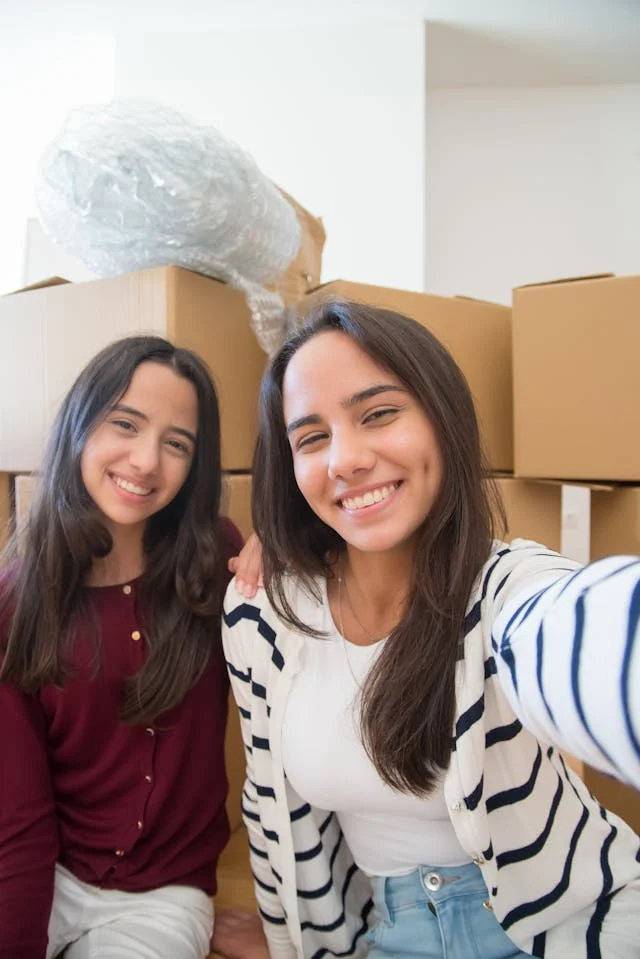 Joyful Moving Day Two young women smiling for a selfie in front of boxes and packing material.