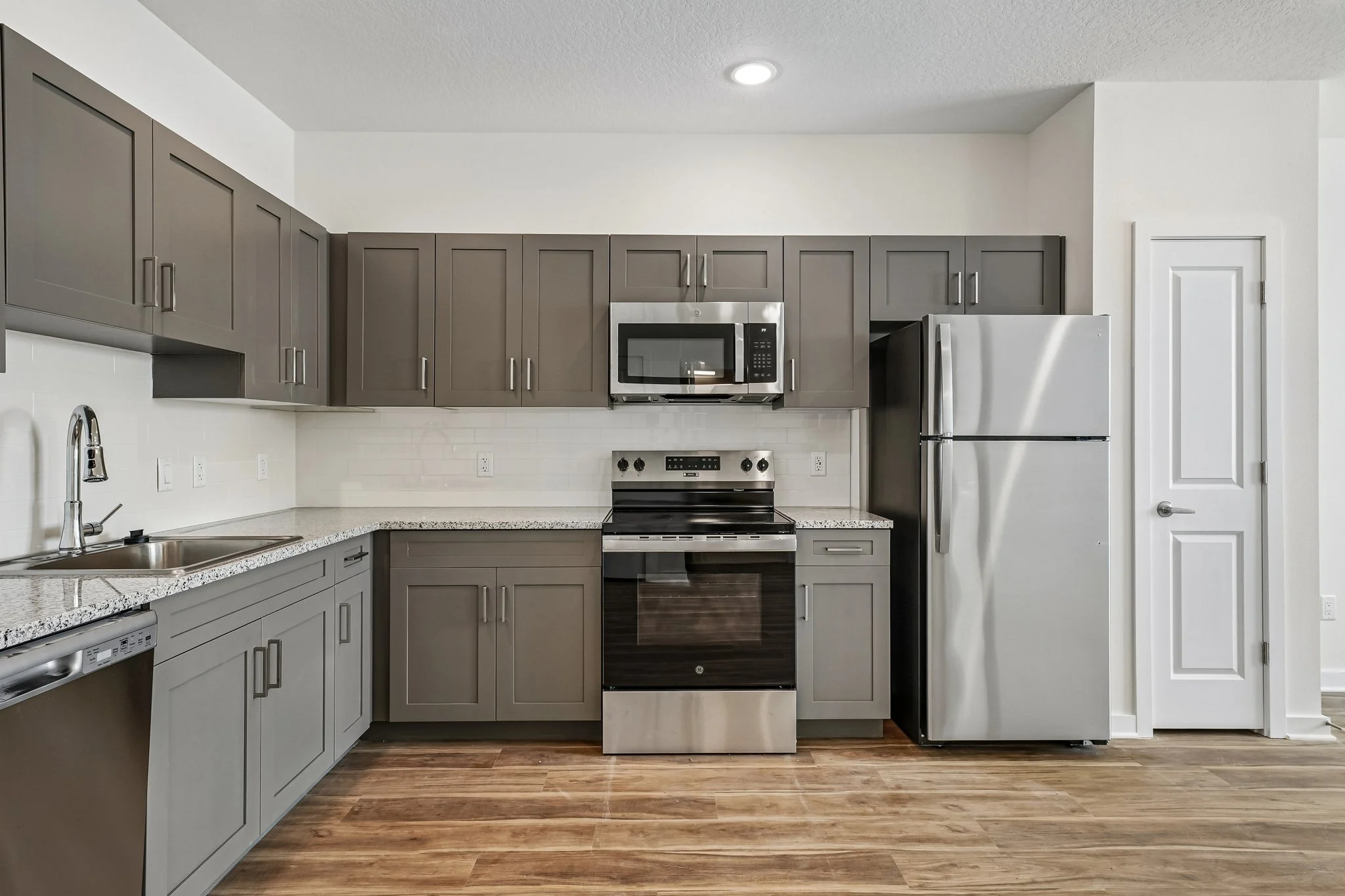 A modern kitchen featuring gray cabinets, stainless steel appliances, and a light-colored backsplash.