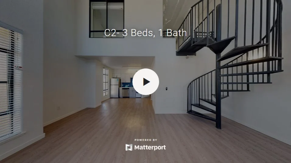 A spacious modern loft interior featuring a spiral staircase, large windows, and light-colored hardwood floors.