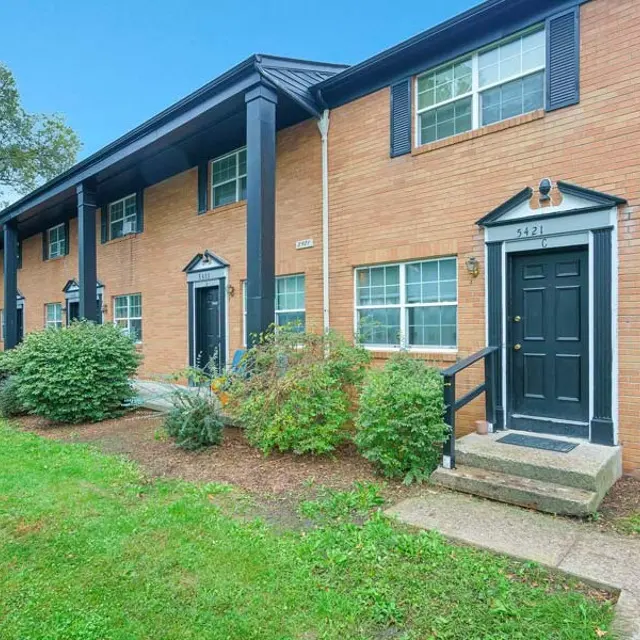 Exterior view of a brick apartment building with black doors and green landscaping.