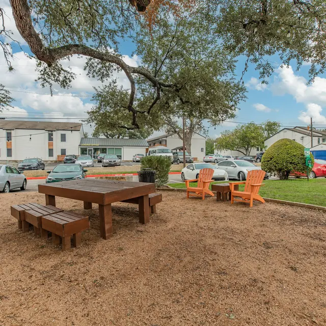 Artisan at South Lamar Picnic table, bench and lounge chairs next to the parking lot at Artisan at South Lamar with trees for natural shade.