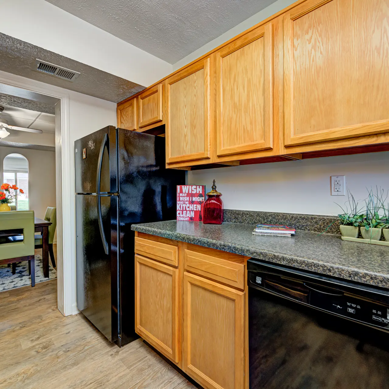 Modern Kitchen Interior A modern kitchen featuring wooden cabinets, a black refrigerator, and a dishwasher, with a granite countertop. In the background, a dining area is visible.