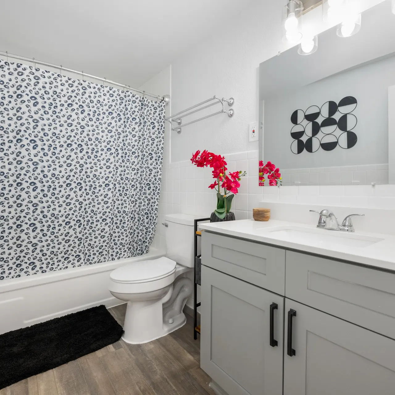 A modern bathroom featuring a bathtub with a decorative shower curtain, a white toilet, a sleek vanity with storage, and decorative plants.