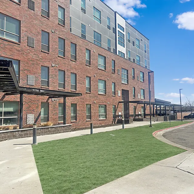 Exterior view of a modern brick building with large windows, featuring a green lawn area in front and a clear blue sky.