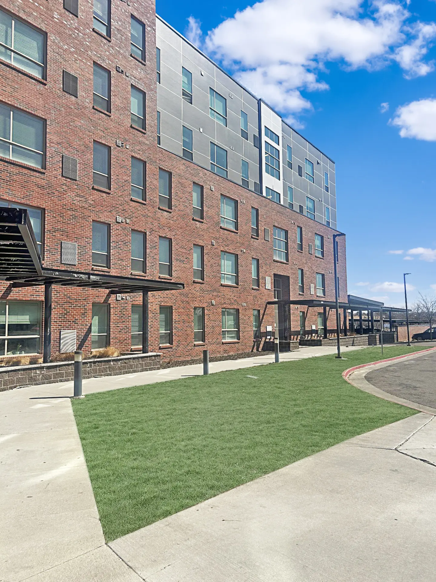 Exterior view of a modern brick building with large windows, featuring a green lawn area in front and a clear blue sky.