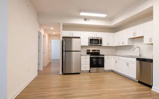 A modern kitchen featuring stainless steel appliances, white cabinetry, and a light wood floor. The layout includes a refrigerator, microwave, oven, and dishwasher with ample counter space.