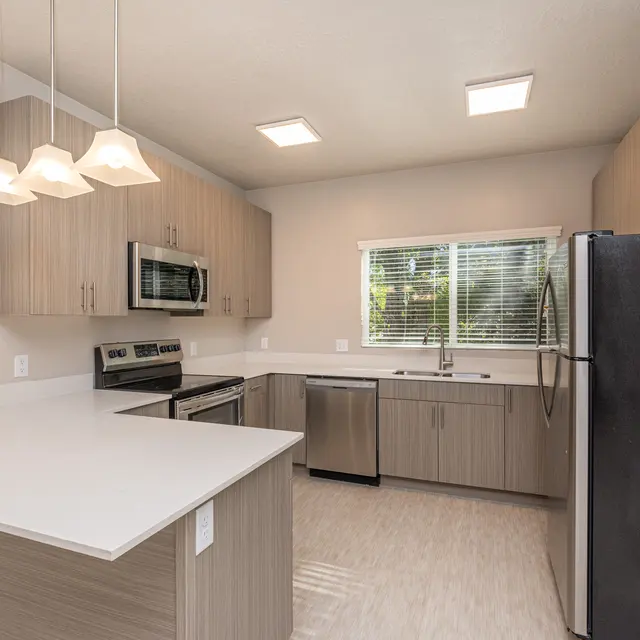 Modern Kitchen Design A modern kitchen with light wood cabinetry, stainless steel appliances, and a white countertop. Bright lighting from ceiling fixtures and a window brings natural light into the space.