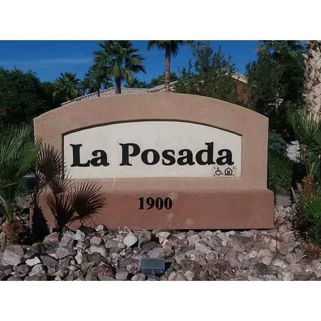 A stone sign with the text 'La Posada' and the number '1900', surrounded by palm trees and desert landscaping.