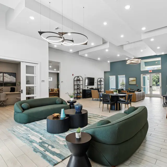 Modern lounge area featuring green sofas, a stylish coffee table, and a dining area with large windows and contemporary decor.