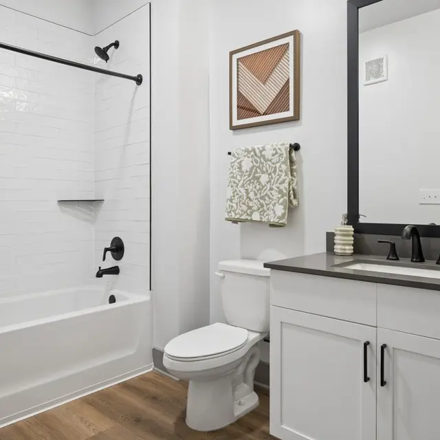 Stylish Modern Bathroom A modern bathroom featuring a white tiled bathtub and shower combination, black fixtures, a white vanity with a dark countertop, and a decorative wall hanging.