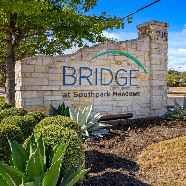 Sign for Bridge at Southpark Meadows featuring stone structure and landscaping.