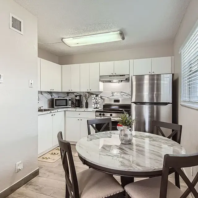 A small kitchen with white cabinets, stainless steel appliances, and a round marble dining table with four chairs