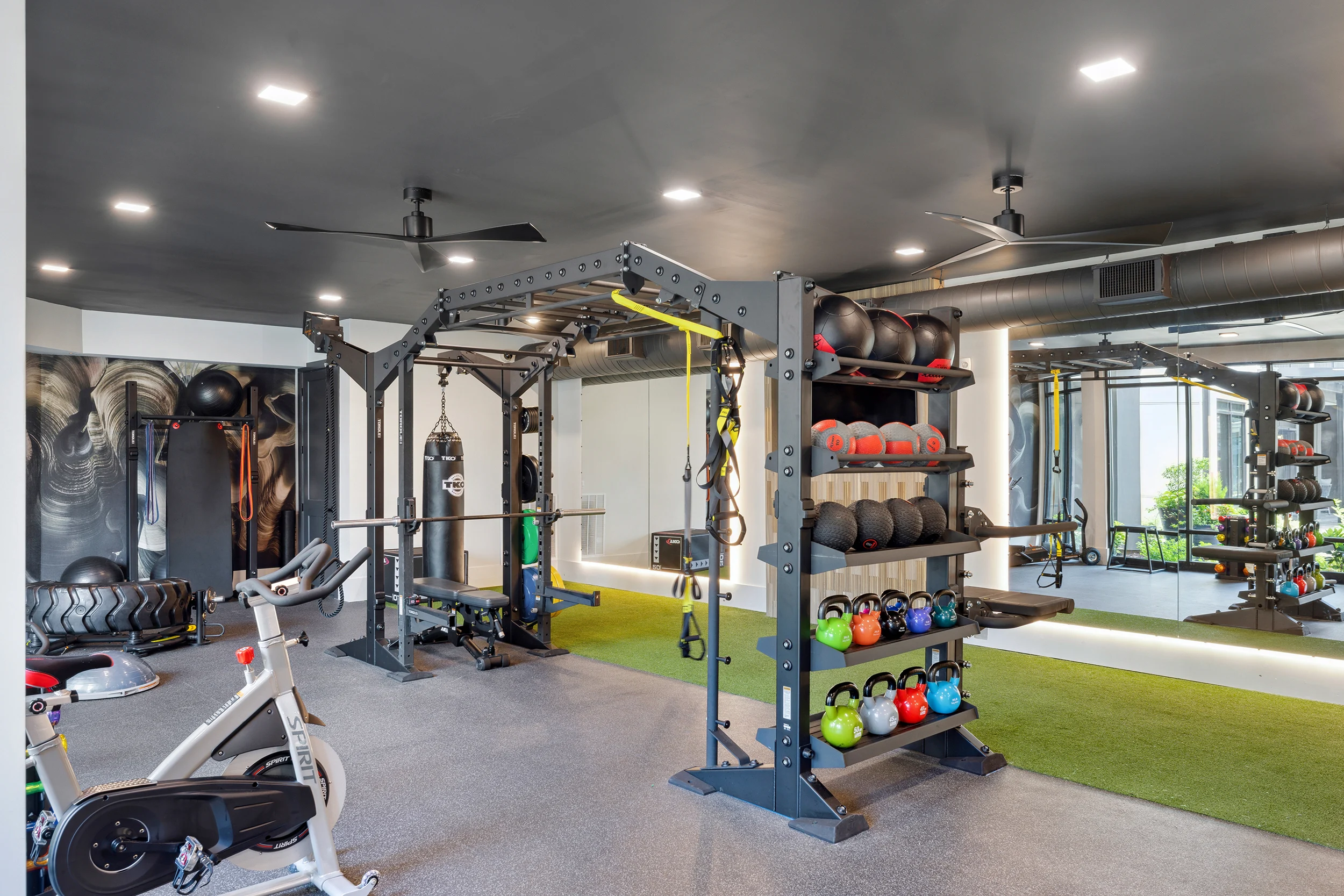 Modern Home Gym Setup A well-equipped modern gym featuring various fitness machines, free weights, and a green turf area. The gym has a sleek design with a black ceiling and colorful workout equipment arranged neatly.