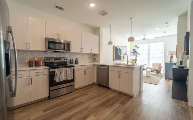 Modern Kitchen Interior A modern kitchen featuring light wood cabinetry, stainless steel appliances, and a central island with seating. The kitchen has a stylish, neutral color palette with wooden flooring and decorative accessories. Natural light flows in from large windows.