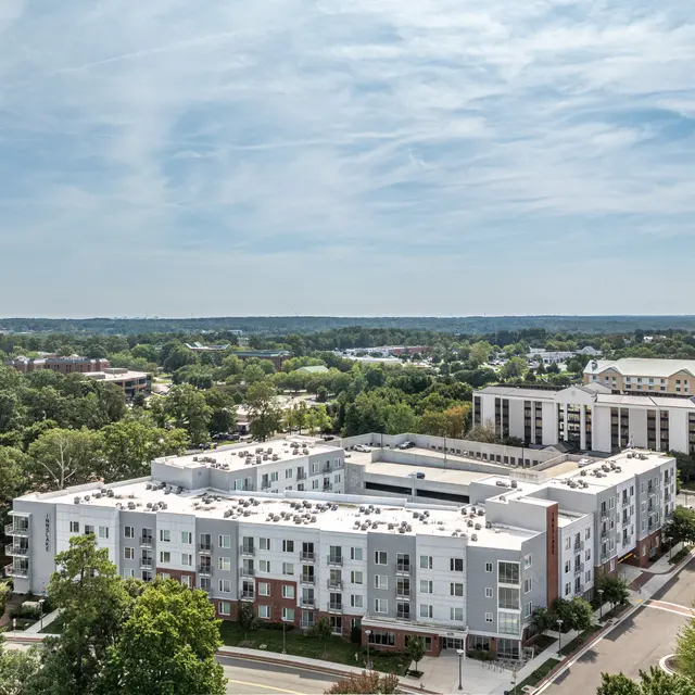 Aerial view of modern multi-story apartments surrounded by green trees and other buildings.