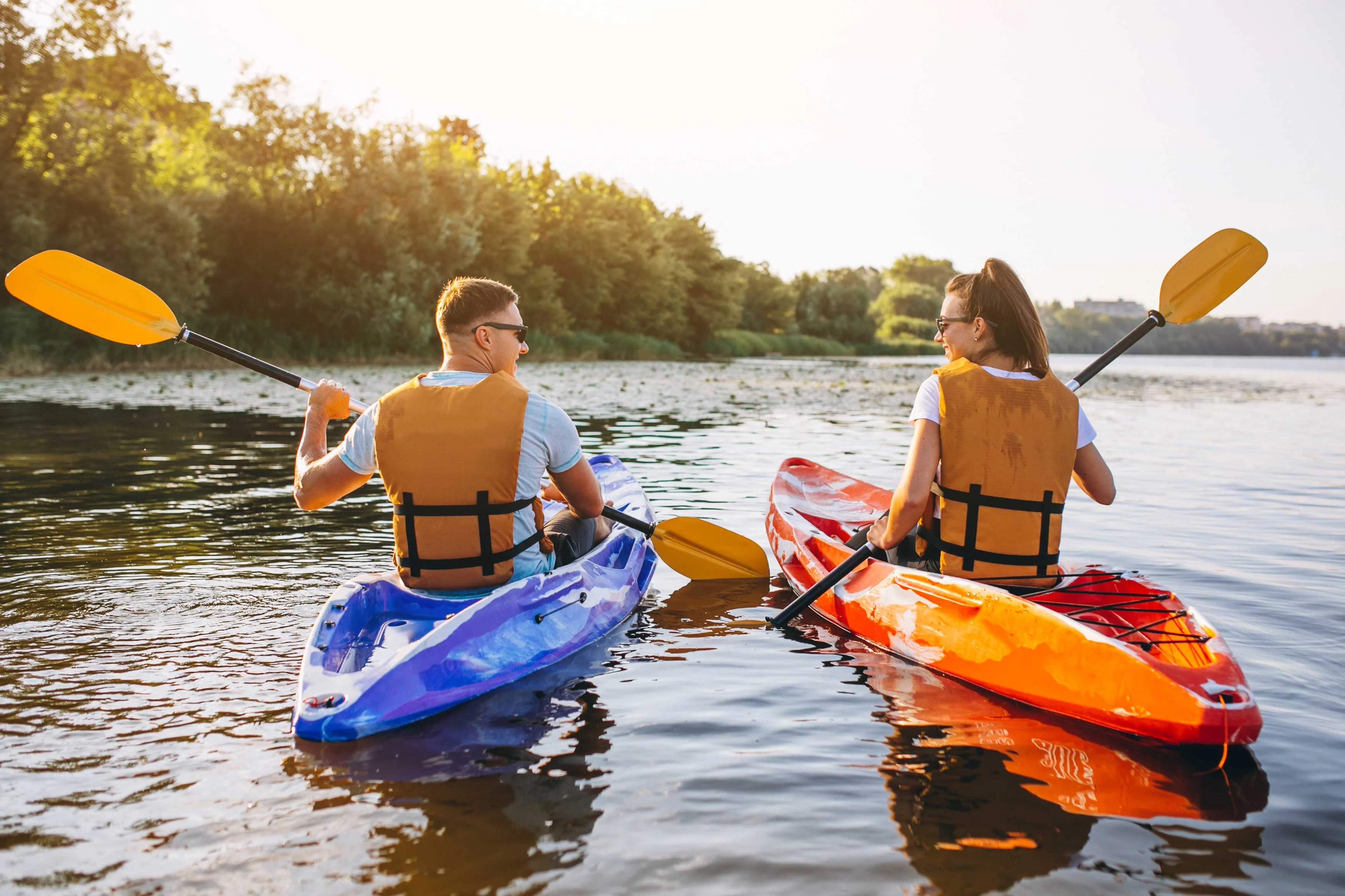 Couple Kayaking on a Sunny Day A man and woman kayaking on a calm river, smiling and paddling with bright yellow paddles in colorful kayaks, surrounded by greenery.