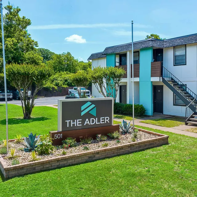 Exterior view of The Adler apartment complex with green lawn and modern sign.