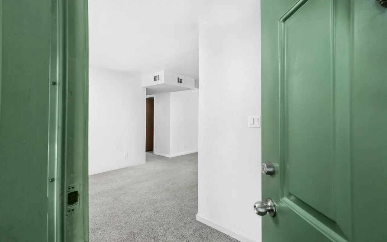 View from an open door into an empty room with light-colored walls and carpet.