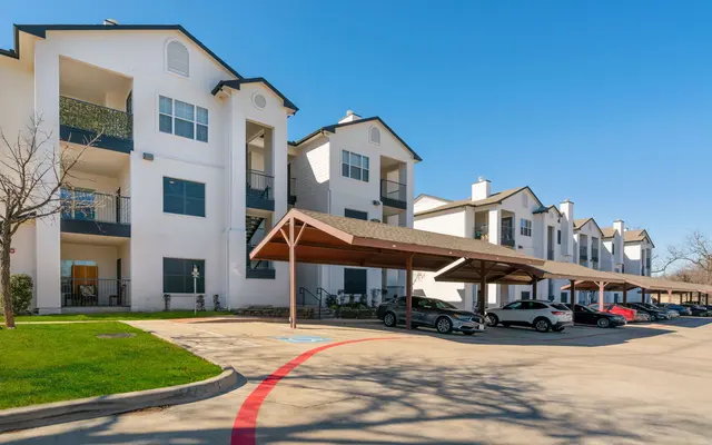Exterior view of a modern apartment complex with white buildings and covered parking areas.