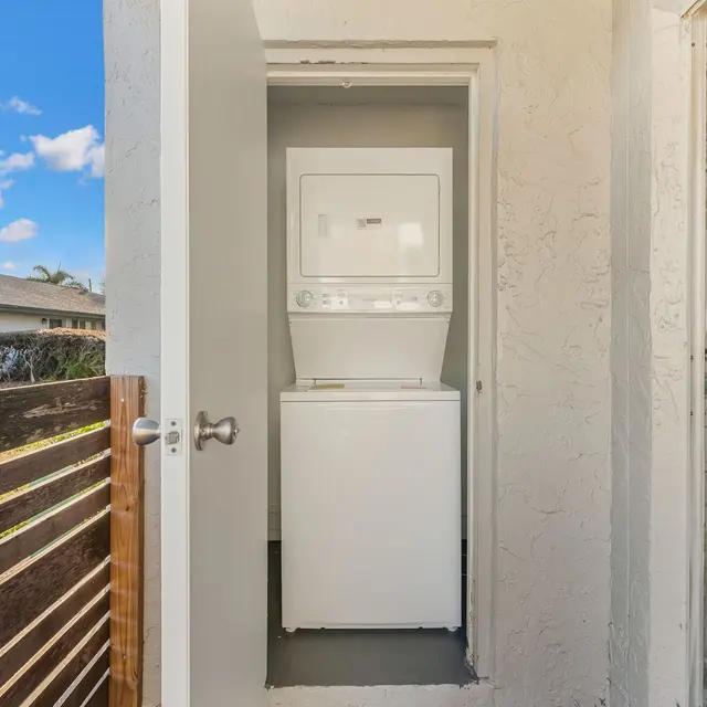 A compact laundry area with a stacked washer and dryer visible through an open door, surrounded by a light-colored wall and a wooden railing.
