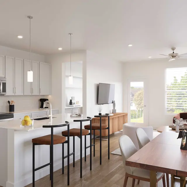 A modern kitchen and living room area featuring a white cabinetry kitchen with an island, bar stools, dining table, and a sofa in a well-lit open-plan layout.