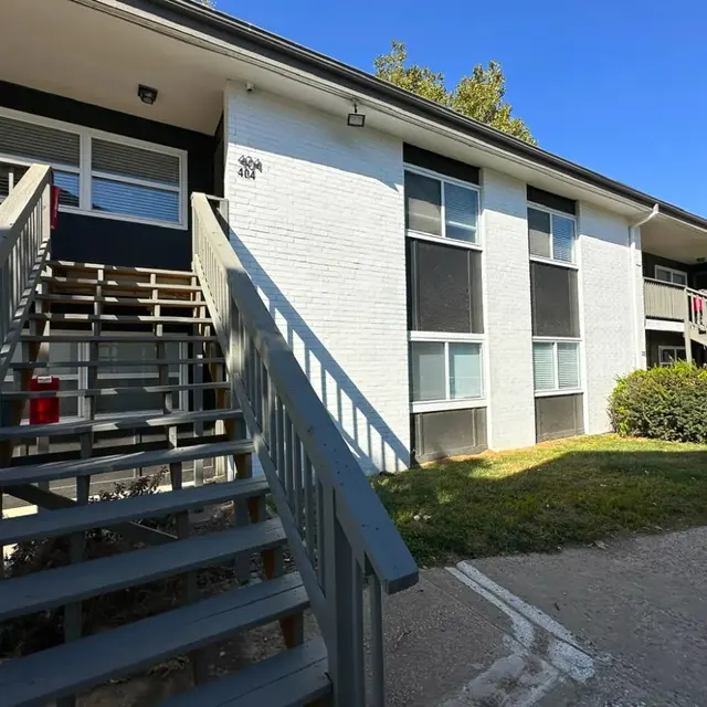 Apartment Building Exterior Exterior view of an apartment building with a wooden staircase, green grass, and blue sky.