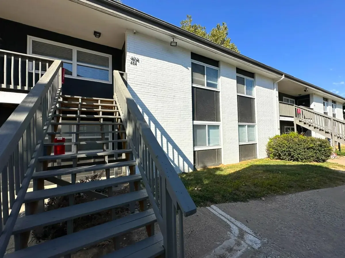 Apartment Building Exterior Exterior view of an apartment building with a wooden staircase, green grass, and blue sky.
