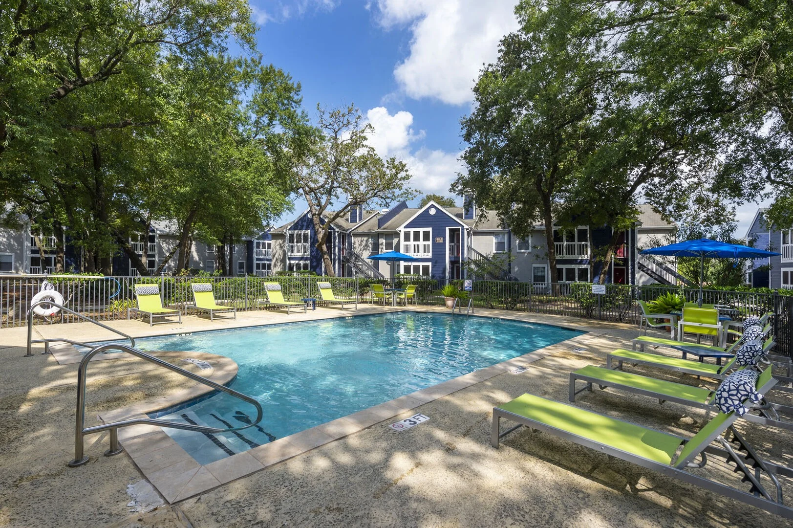 Swimming pool surrounded by green chairs and plants at an apartment complex.