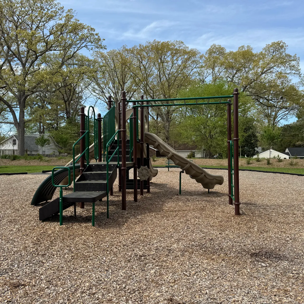 An empty playground featuring a slide, climbing structure, and surrounding gravel ground.