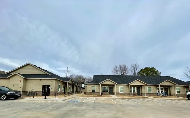 A view of a residential complex featuring several single-story buildings with a cloudy sky above.